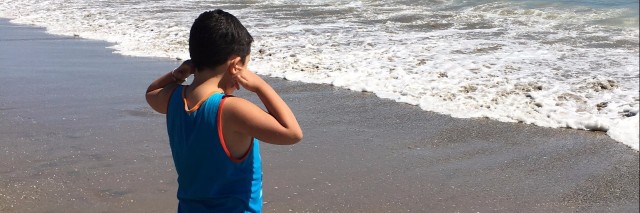 little boy with autism covering his ears at the beach