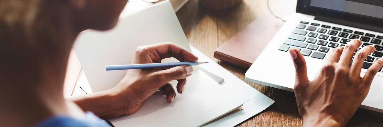 Why We Need Paid Family and Medical Leave in the U.S. woman typing on laptop with one hand with a pen in the other