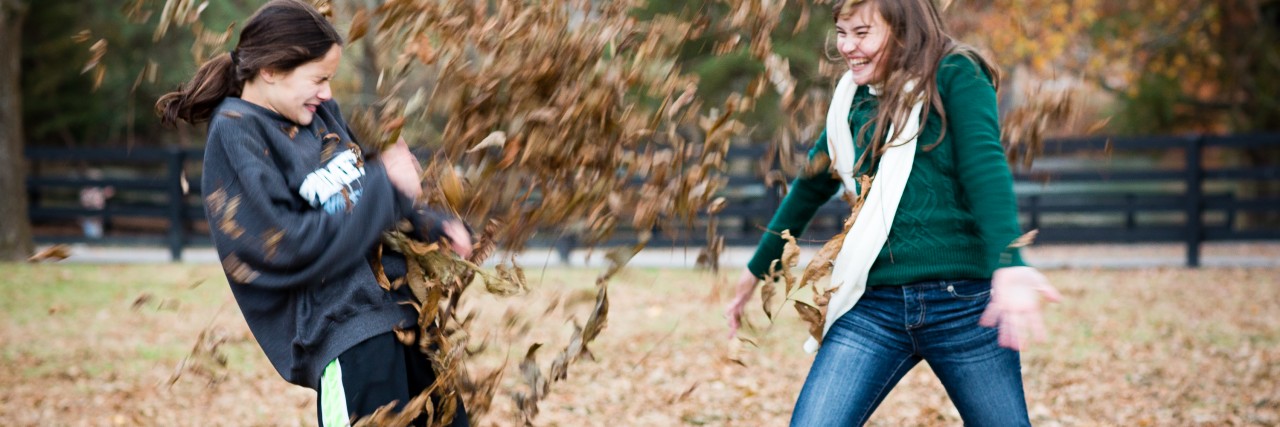 Two girls playing in the autumn leaves outdoors