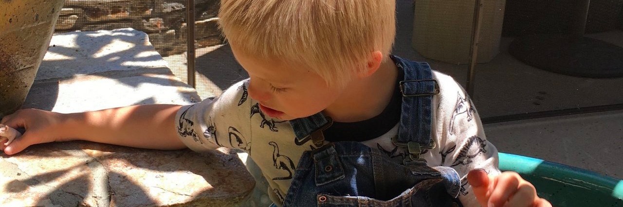 The Moment My Son With Down Syndrome Was Also Diagnosed With Autism boy in overalls sits outside near a pool