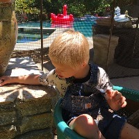 boy in overalls sits outside near a pool