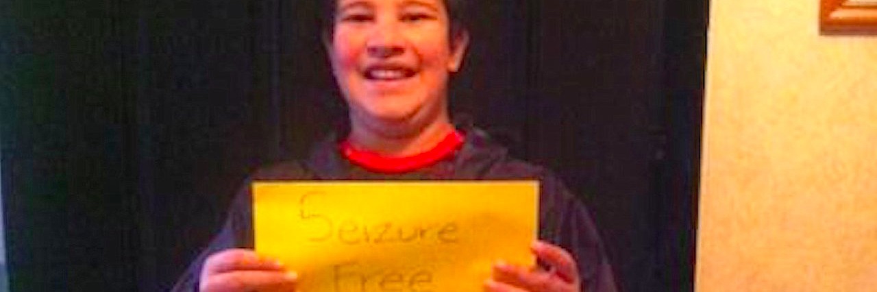 Boy holds up sign that says, “Seizure free for 100 days.”