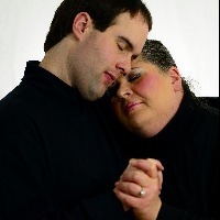 Man and woman holding hands, with woman head on man's shoulder, both of their eyes closed