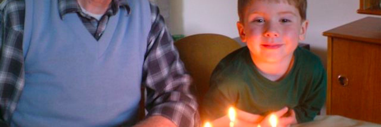 the author's dad and her young son sitting in front of a birthday cake with lit candles