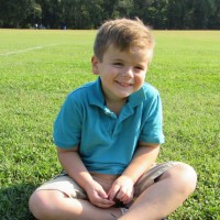 Boy in a blue polo shirt, sitting on the grass