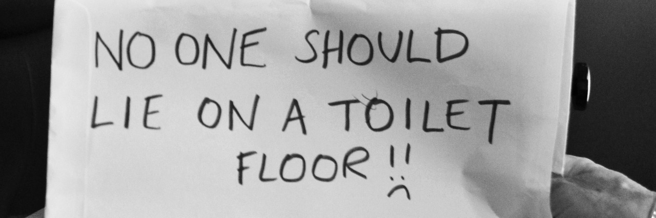 Boy with sign saying "No one should lie on a toilet floor!"