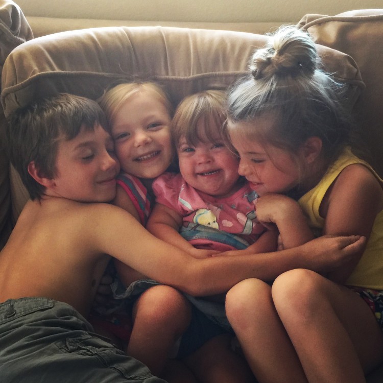 four young children hugging together on a couch