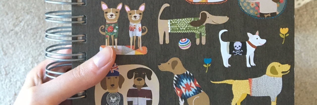 Pulmonary Hypertension: Keeping a Gratitude Journal to Stay Positive woman holding journal with dogs on the cover with her dog lying in the background