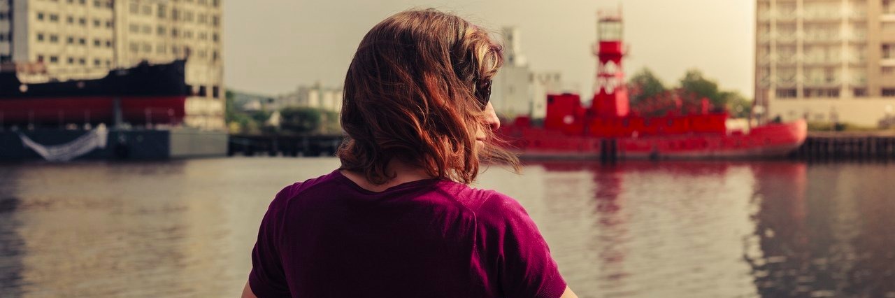 Forgiving the People Who Bullied Me Because of My Autism Young woman relaxing by river and looking across at buildings