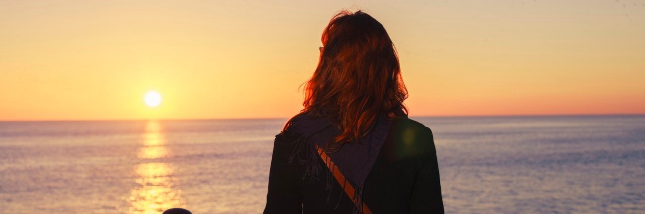 The One Chronic Illness Symptom I Wish I Could Get Rid Of Woman admiring the sea at sunset