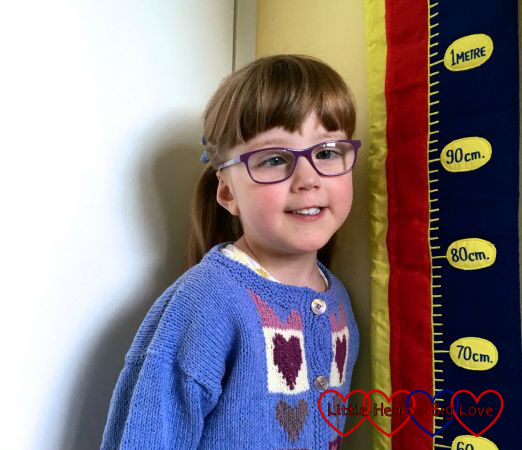 Jessica wearing her heart jumper and standing next to the measuring chart on her wall