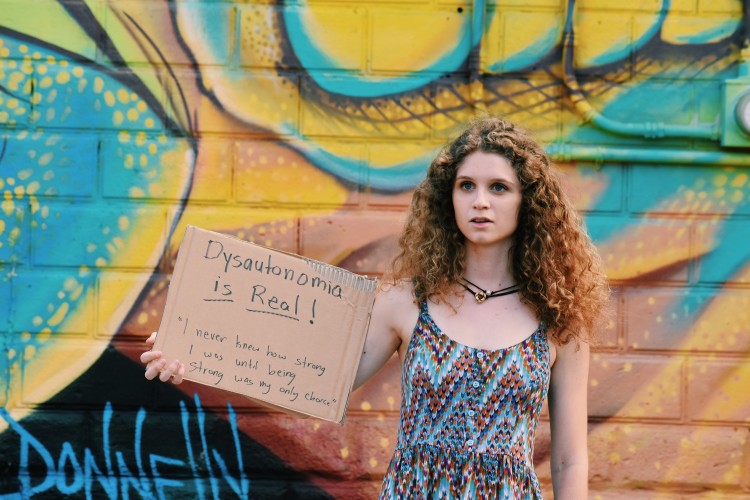 a woman holds a sign that says dysautonomia is real! i never knew how strong i was until being strong as my only choice