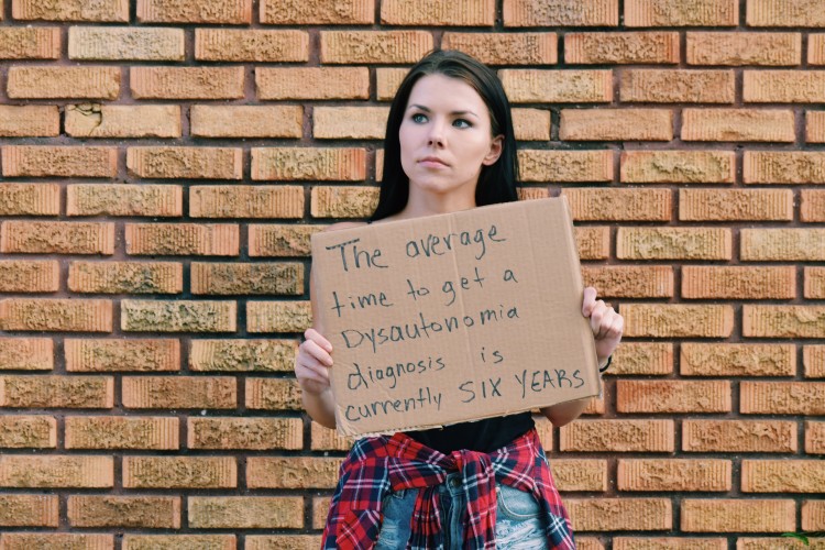 a woman holds a sign that says the average time to get a dysautonomia diagnosis is currently 6 years