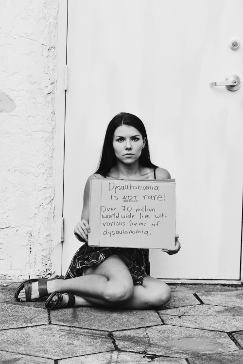 a woman sits on the ground holding a sign that says dysautonomia is not rare. over 70 million worldwide live with various forms of dysautonomia