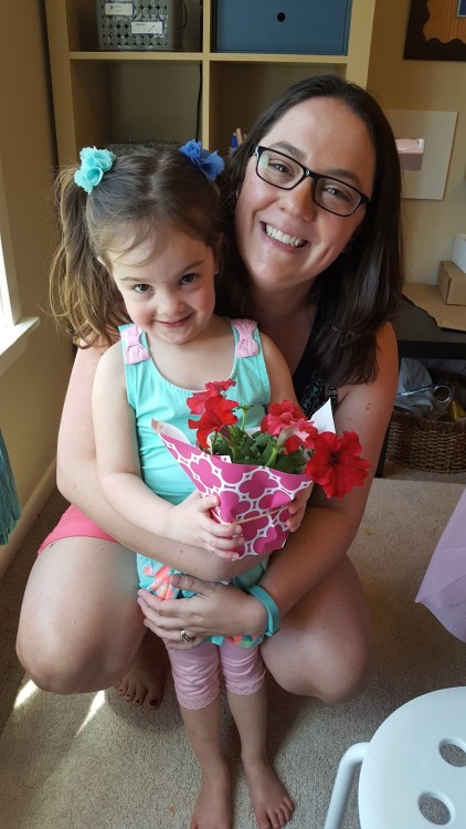 A mom holding her daughter, who is holding flowers.