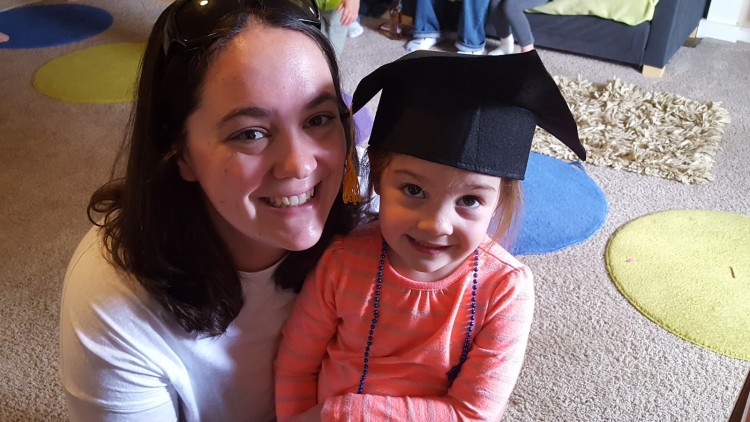 A mom and her daughter, who is sitting on her lap, looking up at the camera