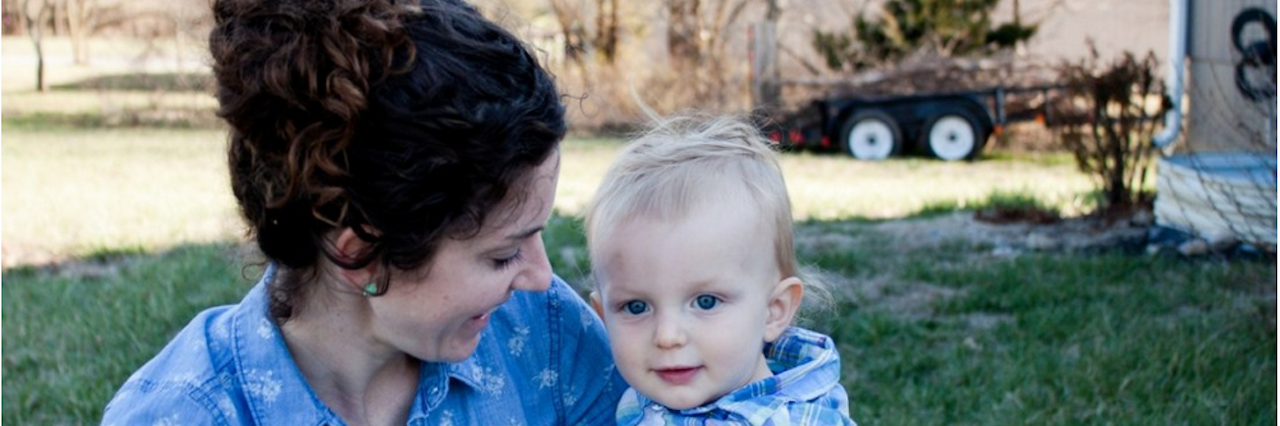 The Good Things That Came From My Postpartum Depression and Anxiety Mom sits on grass and smiles at baby boy