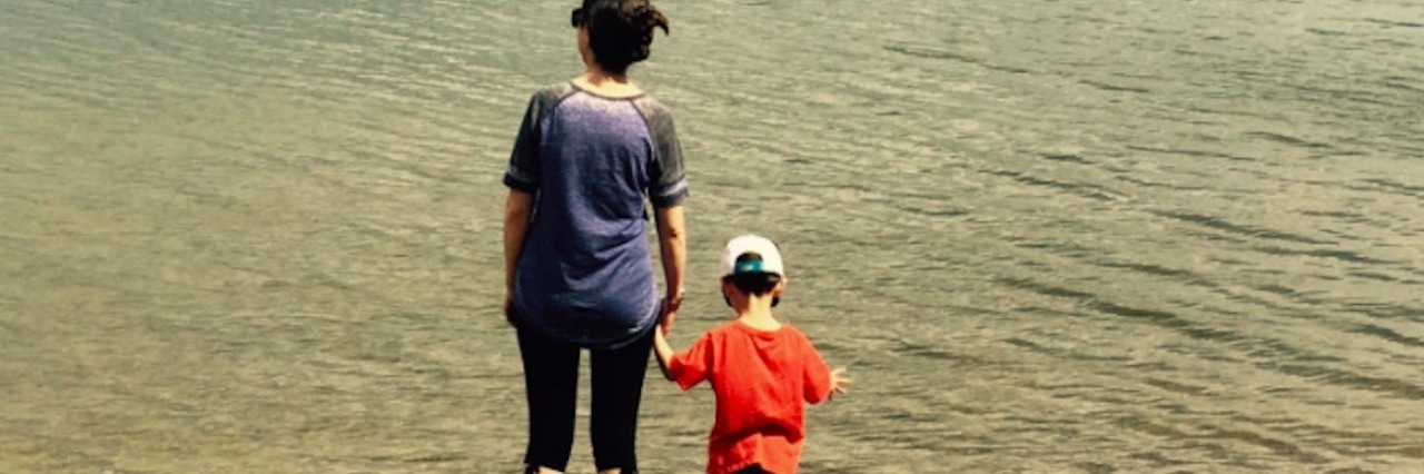 A woman and child holding hands, standing at the shore