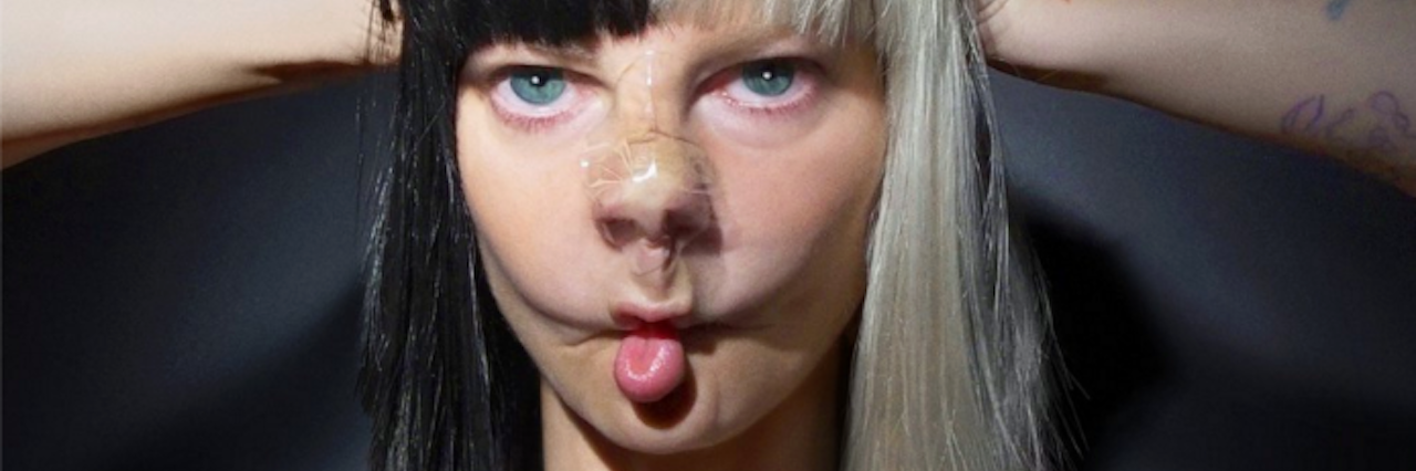 A photo of a young woman with tape on her nose and her hands on top of the half black, half white wig on her head