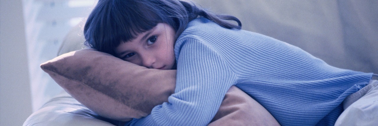 young girl hugging cushion while laying on sofa