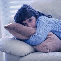 young girl hugging cushion while laying on sofa