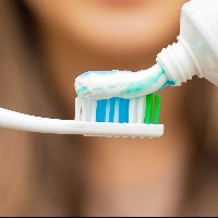 Young woman holding a toothbrush and placing toothpaste on it.