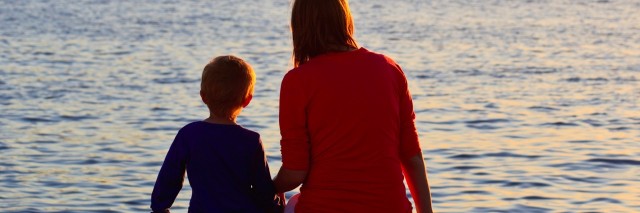 Mom and son sitting near water, looking at sunset landscape
