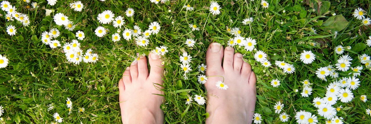 Female feet standing on green grass and white flowers