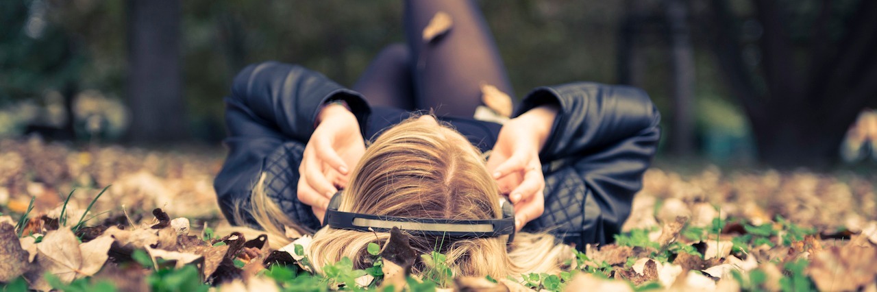 Songs to Helps Ease Anxiety woman with her headphones in laying in a pile of leaves