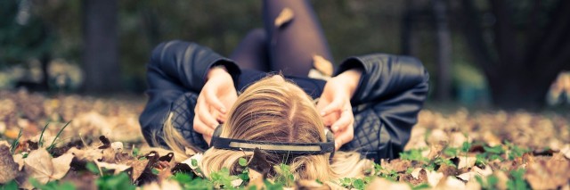 woman with her headphones in laying in a pile of leaves