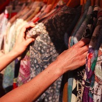 woman's hands looking at shirts hanging on rack