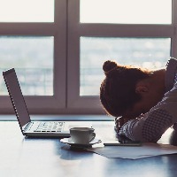 woman with her head down on the table sitting in front of her laptop