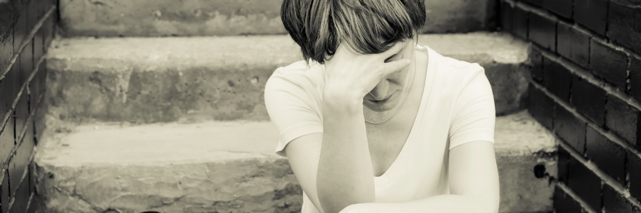What 'I'm Having a Bad Day' Means as Someone Who's Sick A woman sits on the concrete stairs in a very depressed mood, lying next to her on the stairs of her backpack.