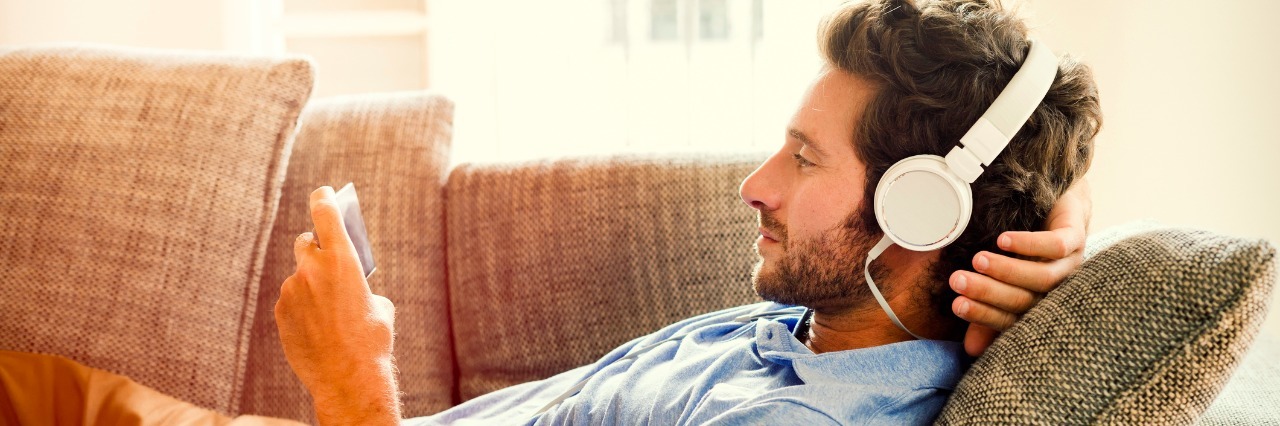 man lying on couch listening to music through headphones