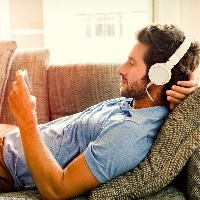 man lying on couch listening to music through headphones