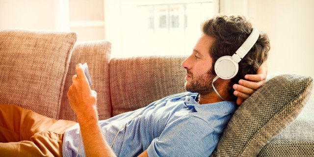 man lying on couch listening to music through headphones