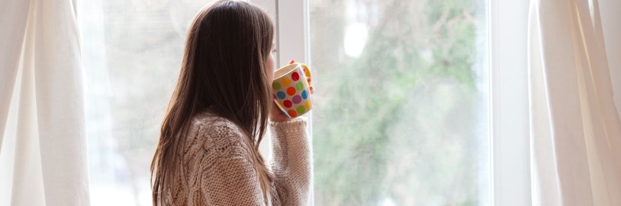 young woman sitting by the window having hot drink