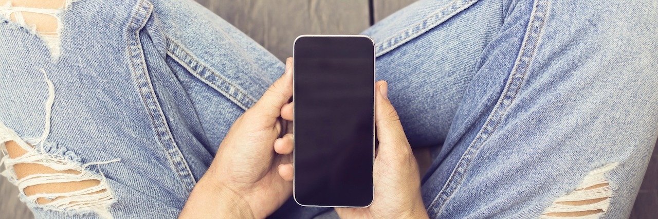 The Benefit of Reaching Out to Friends When You're Depressed A woman sitting cross-legged and holding her phone in her lap