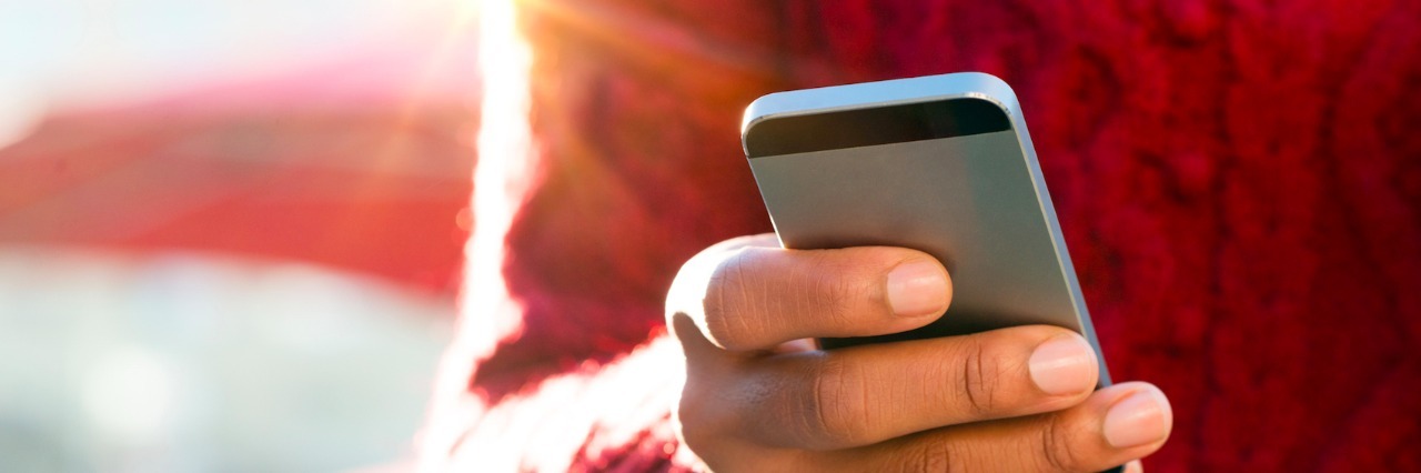 A Letter to the People Who Share Stories on The Mighty Close up of hand of person wearing red sweater, holding phone