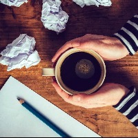 woman holding a cut of coffee with a pen and crumpled up pieces of paper on her desk