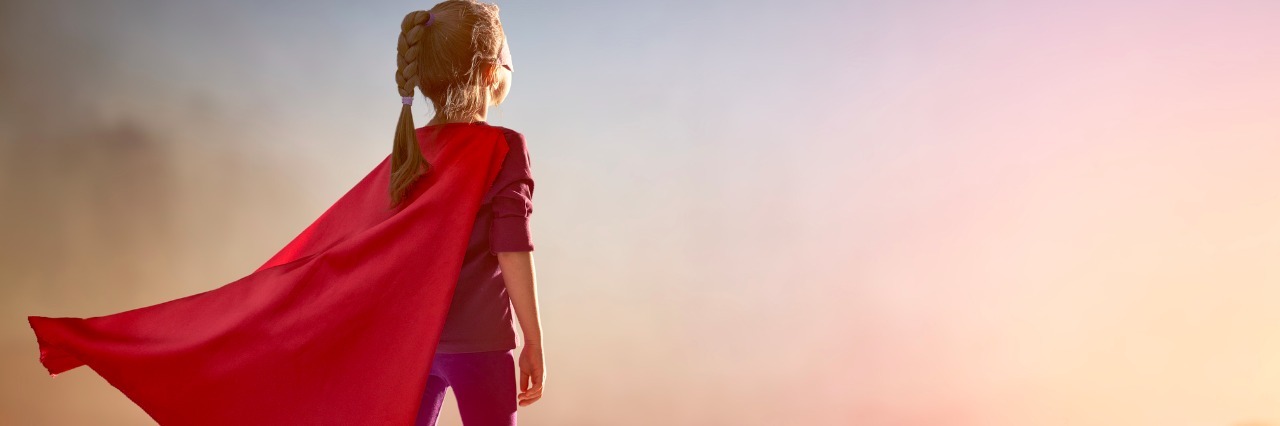Why Health Issues Feel Like Wearing a Superhero Costume girl standing on building wearing a red superhero cape