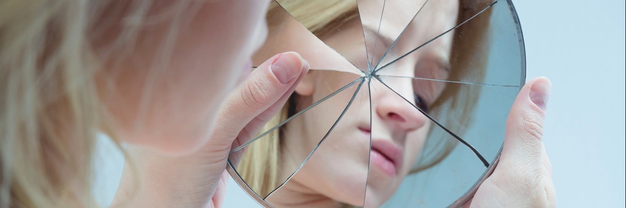 a young woman looking at herself in a cracked mirror