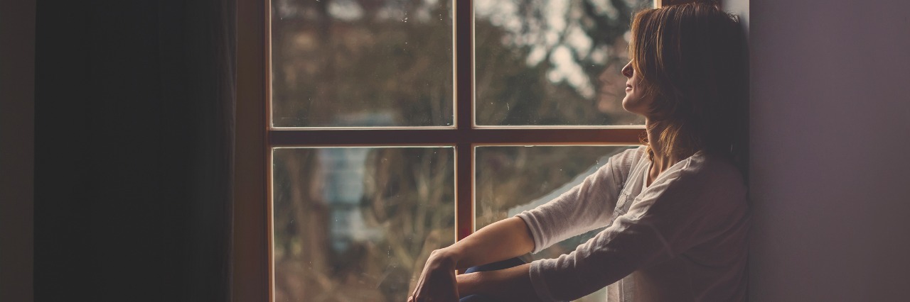 Not Feeling Motivated to Get Through a Fibromyalgia Flare Young attractive woman, sitting on a window, looking outside, lonely mood