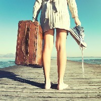 woman standing on a dock holding her shoes and a suitcase
