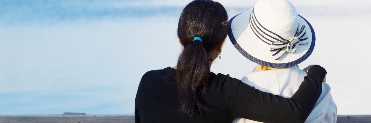 Fibromyalgia Symptoms in Families older woman and adult daughter sitting on wooden dock looking at lake