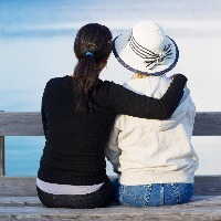 older woman and adult daughter sitting on wooden dock looking at lake