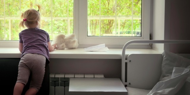 Little girl in a hospital ward looking at spring greens through the window and waiting for her parents to come