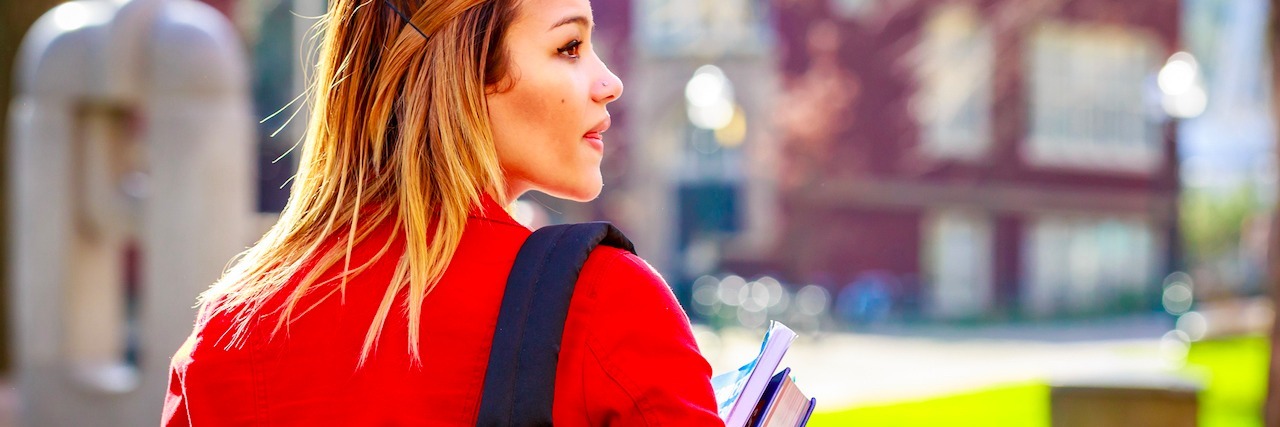 college student walking through campus with books and her backpack