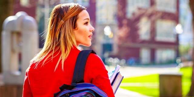 college student walking through campus with books and her backpack