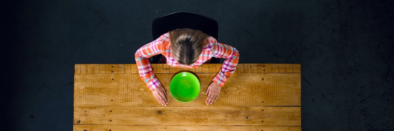 top view of girl sitting at table with an empty green plate